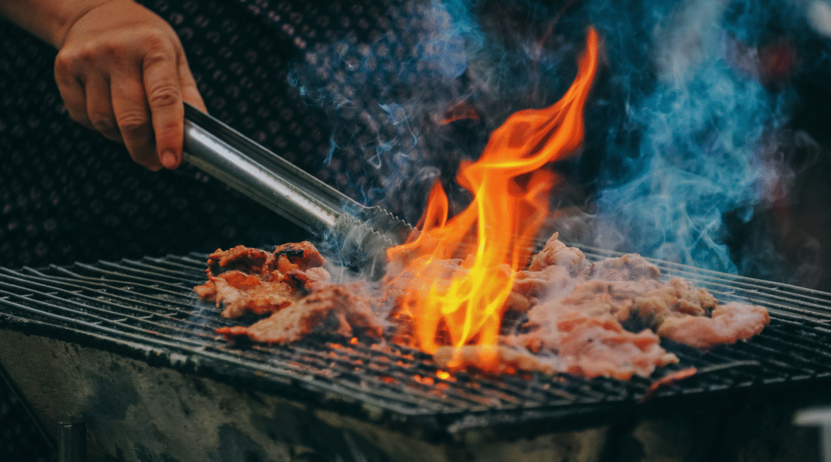 meat cooking over grill with large flame