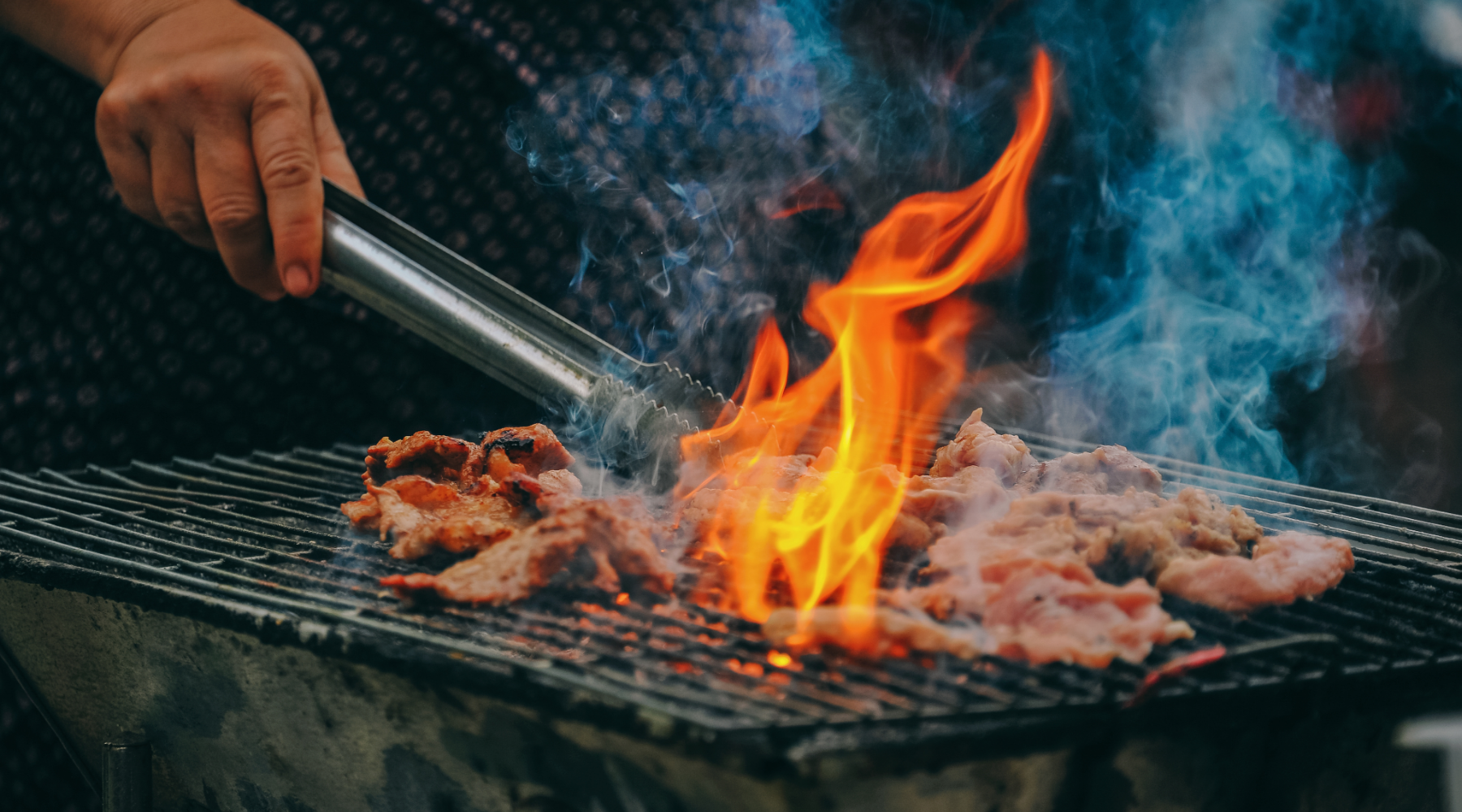 meat cooking over grill with large flame