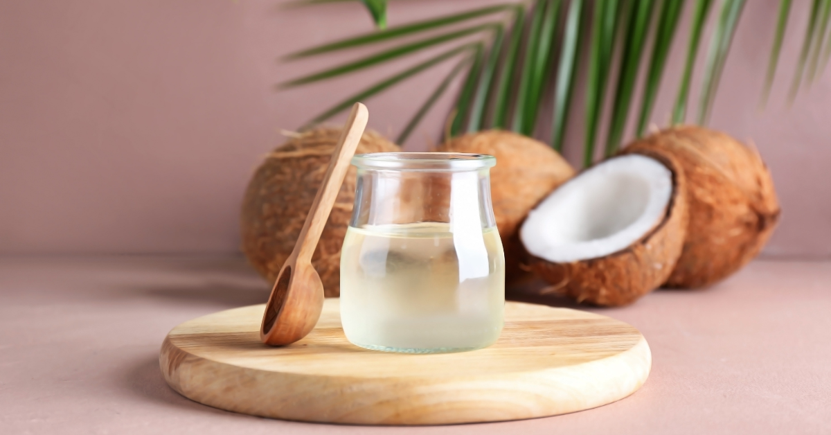 glass of coconut oil on wood tray in front of coconuts